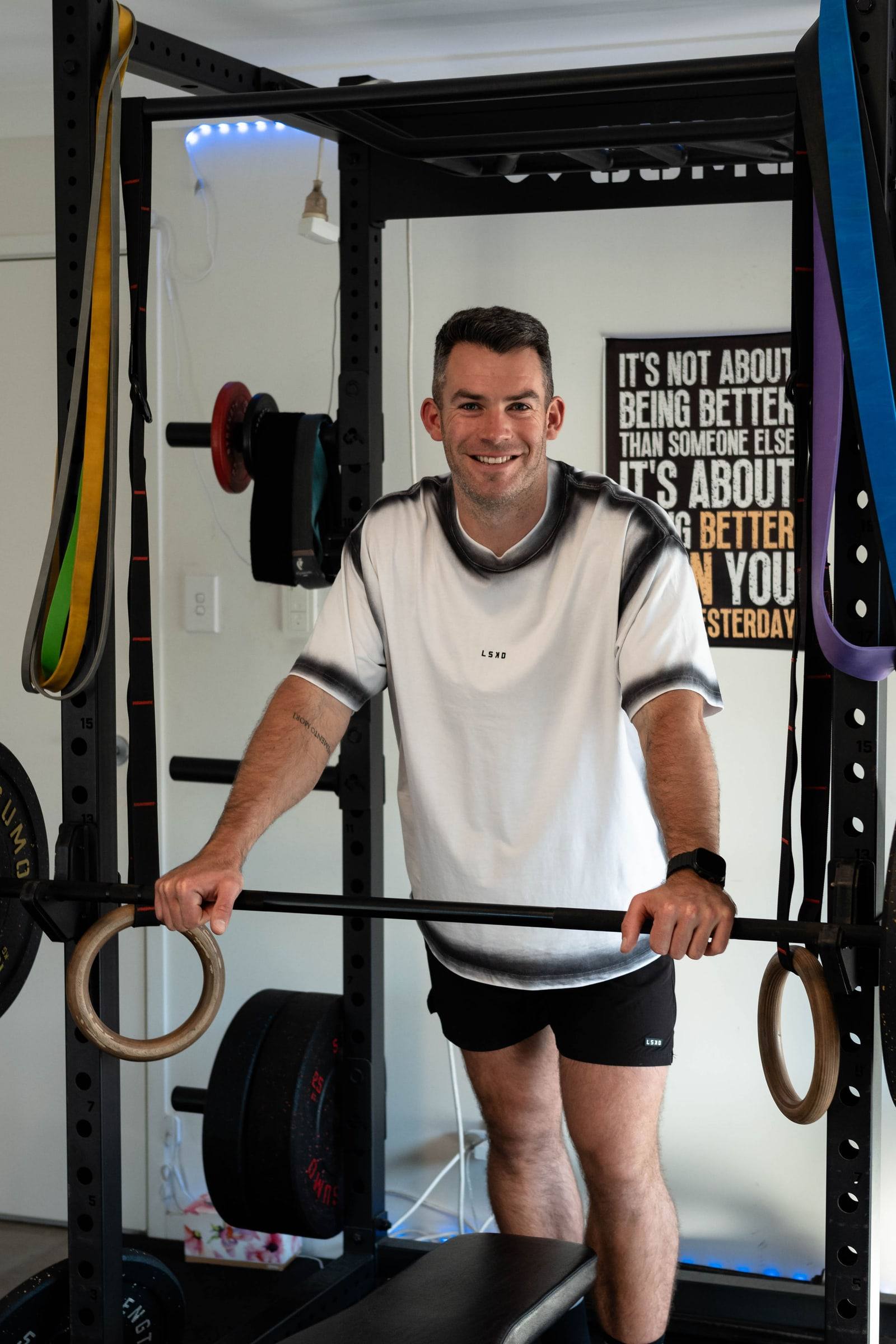 Richy smiling beside a loaded barbell in the home gym