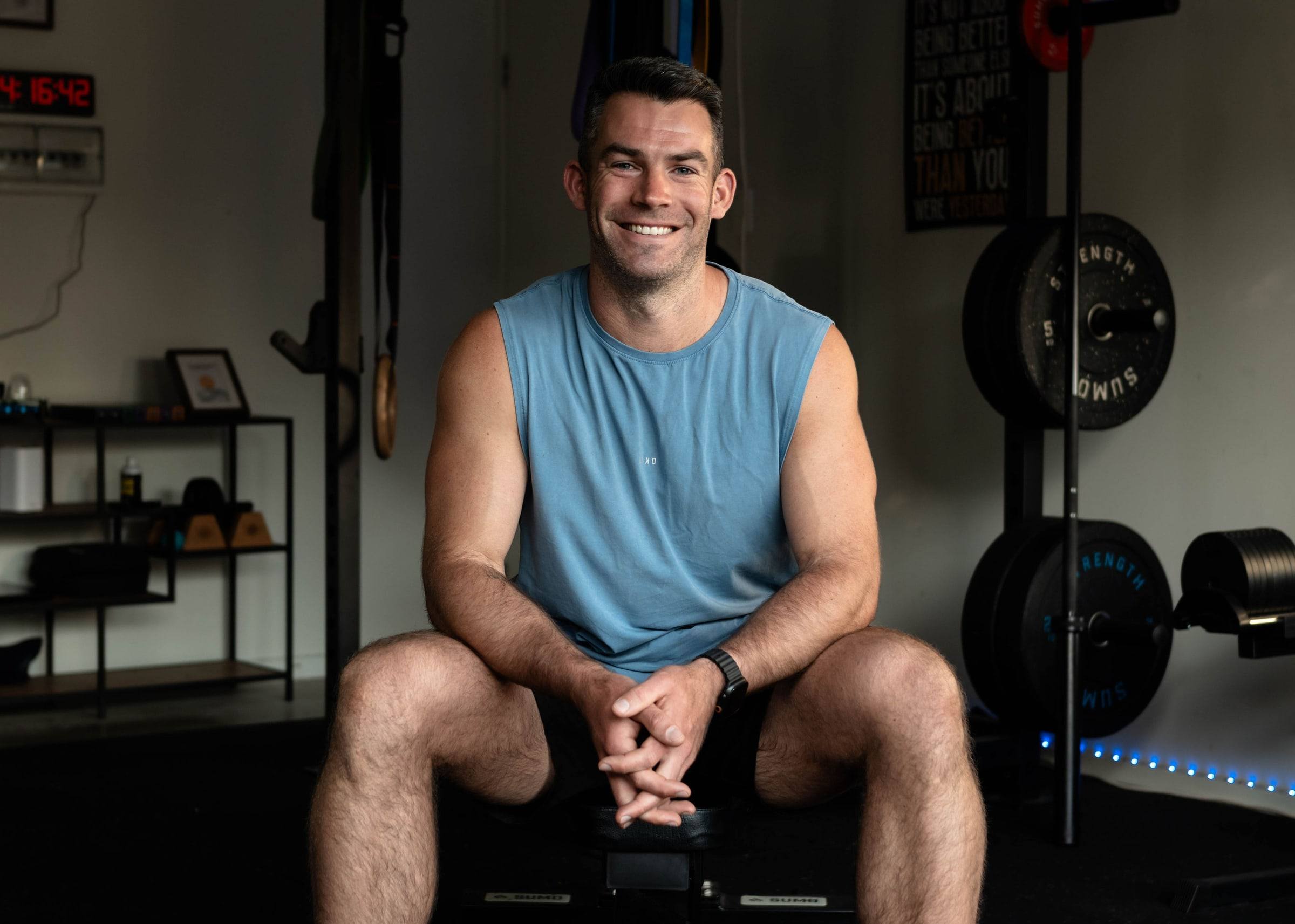 Richy sitting on a bench in the home gym, smiling