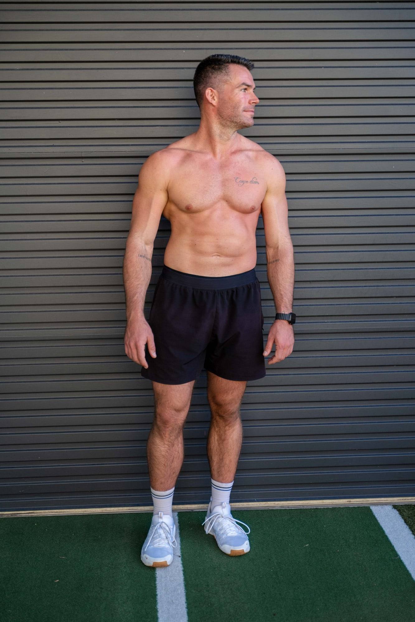 Richy standing against a grey roller door on the turf outside the gym, looking to the side